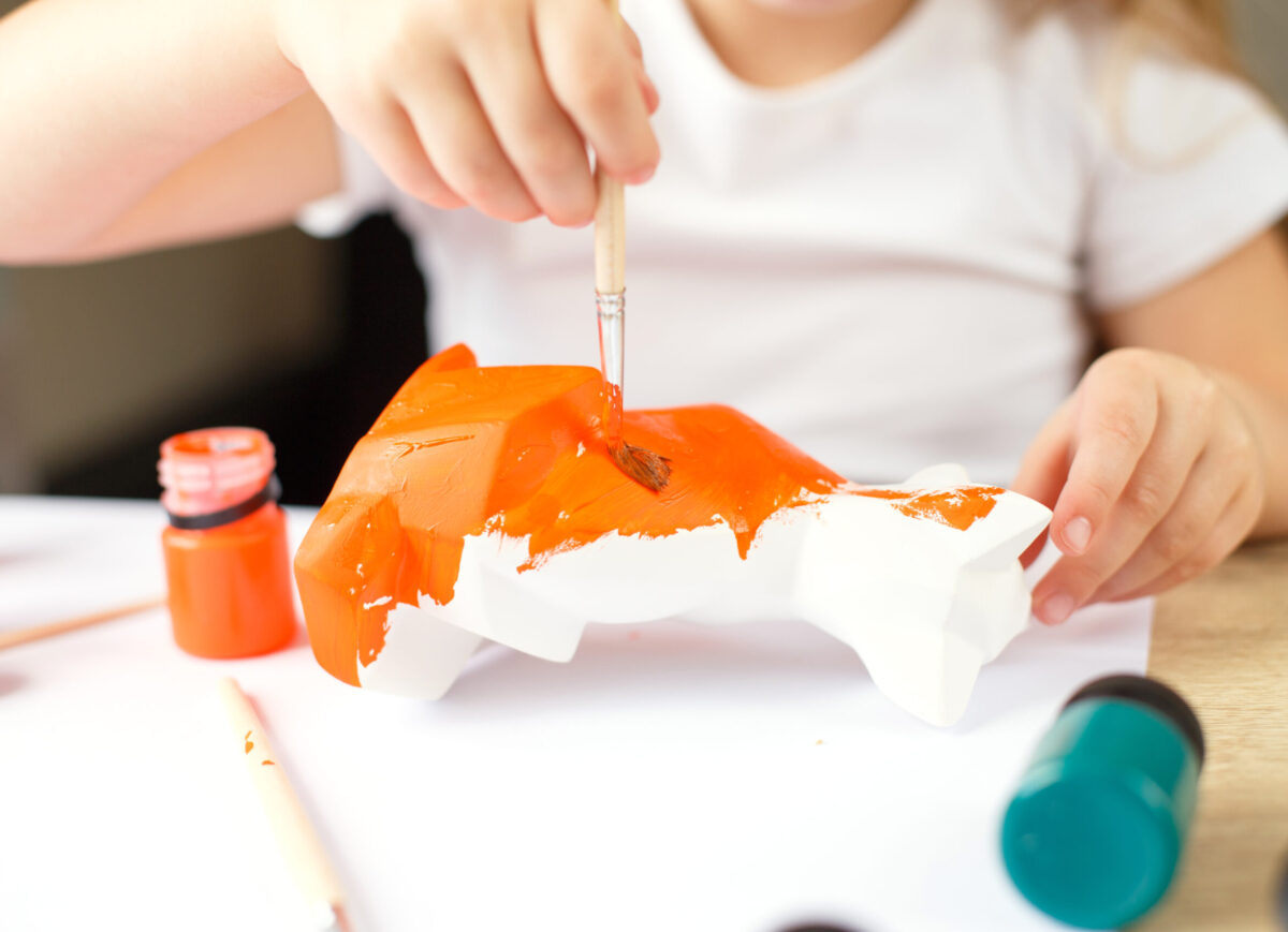 a little girl paints a toy fox made of clay. DIY concept.