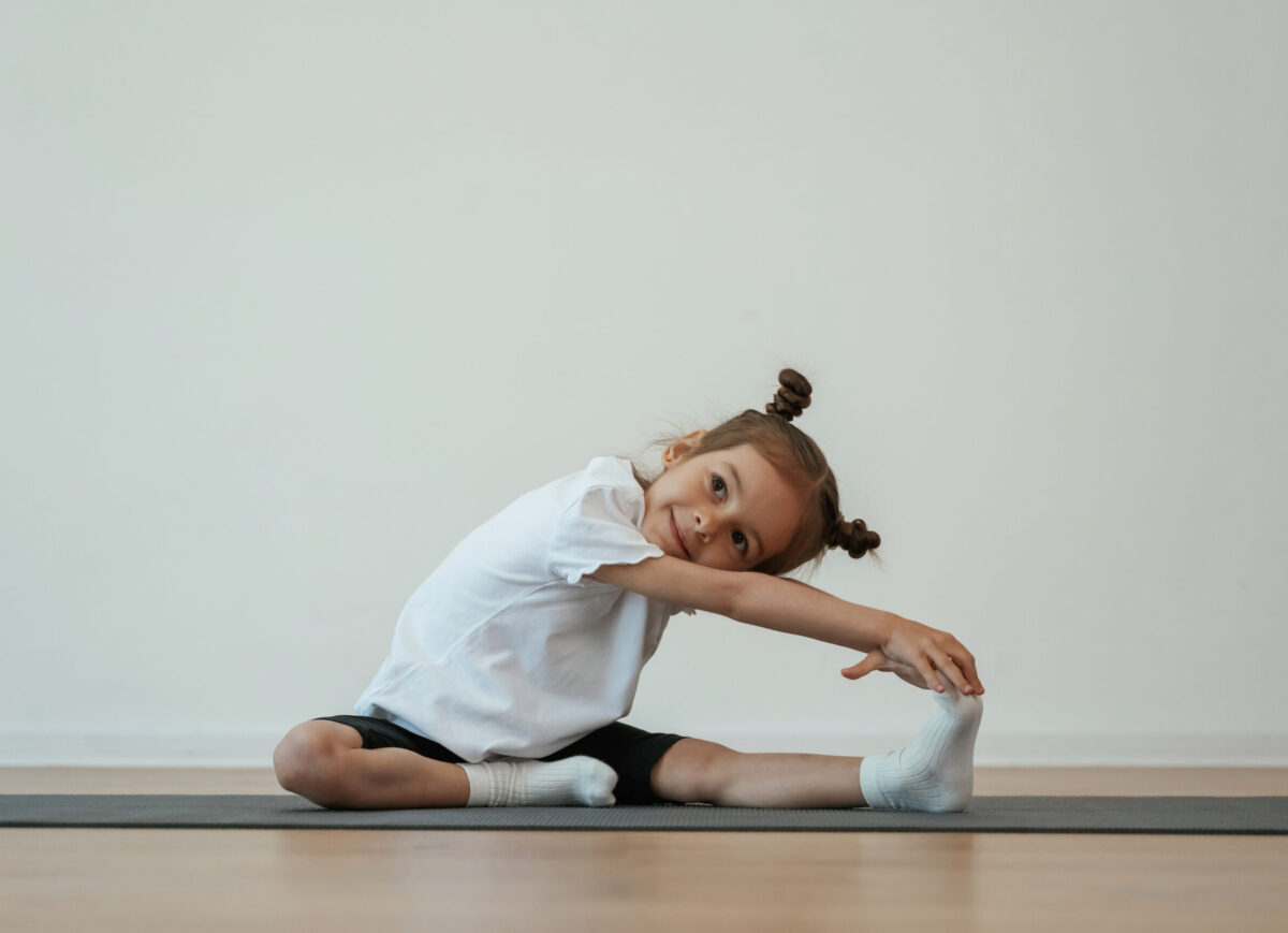 Stretching the leg. Cute little girl is sitting on the yoga mat and doing exercises.