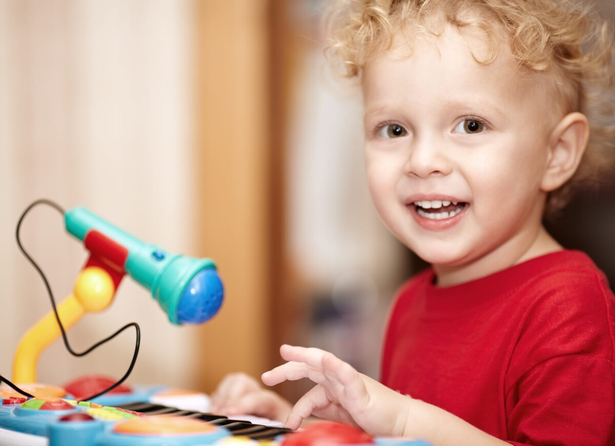 Adorable little boy with a mischievous smile and curly blond hair playing with a colourful plastic toy microphone