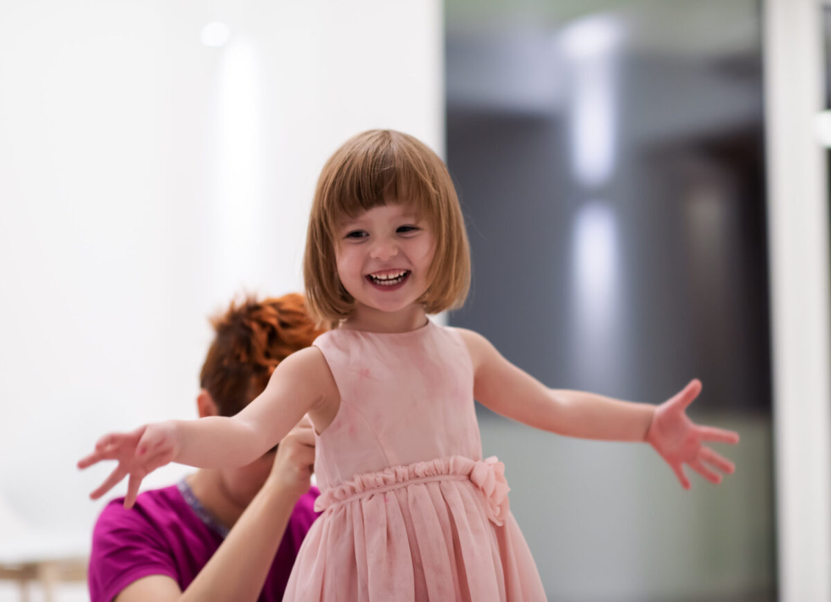 family having fun on beutiful evening at home young mother helping cute little daughter while putting on a pink dress for dancing at home